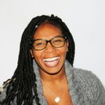 A vibrant portrait of a smiling woman with dreadlocks and glasses, exuding joy.